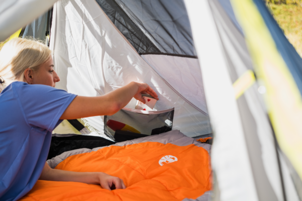 Young man reaching for playing cards while laying on a Silverton sleeping bag in a coleman tent