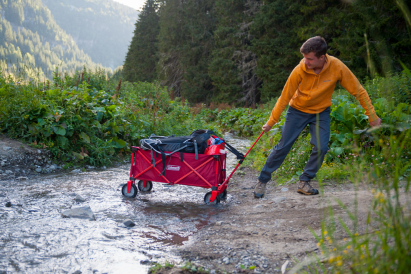 Loaded Coleman Camping Wagon being pulled through water by a Young man.