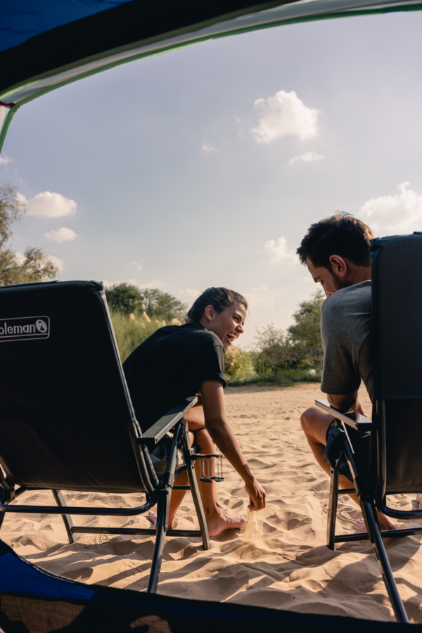 Young couple enjoying the sunshine in the cofort of their Coleman camping chairs.